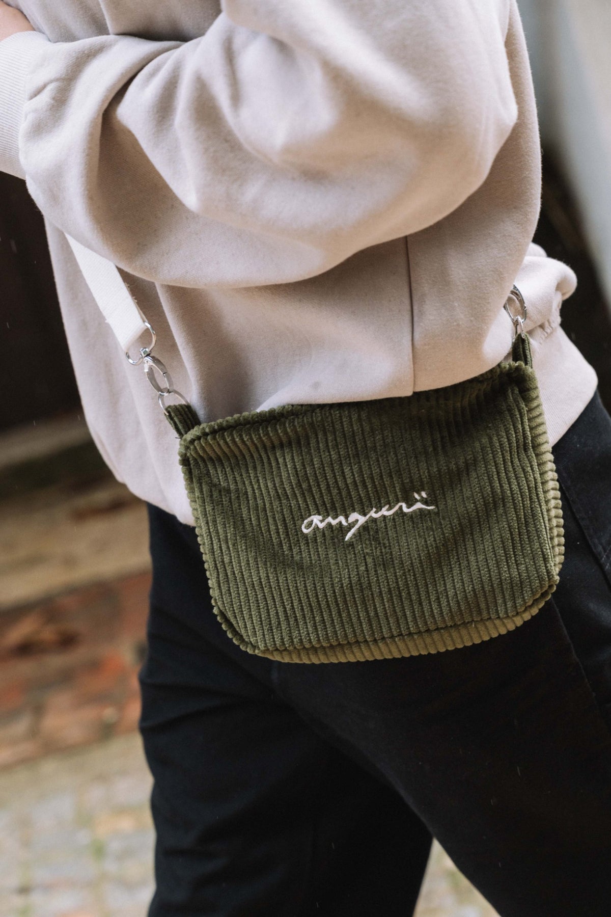 Khaki corduroy crossbody bag with white angurä embroidery, worn across the body
